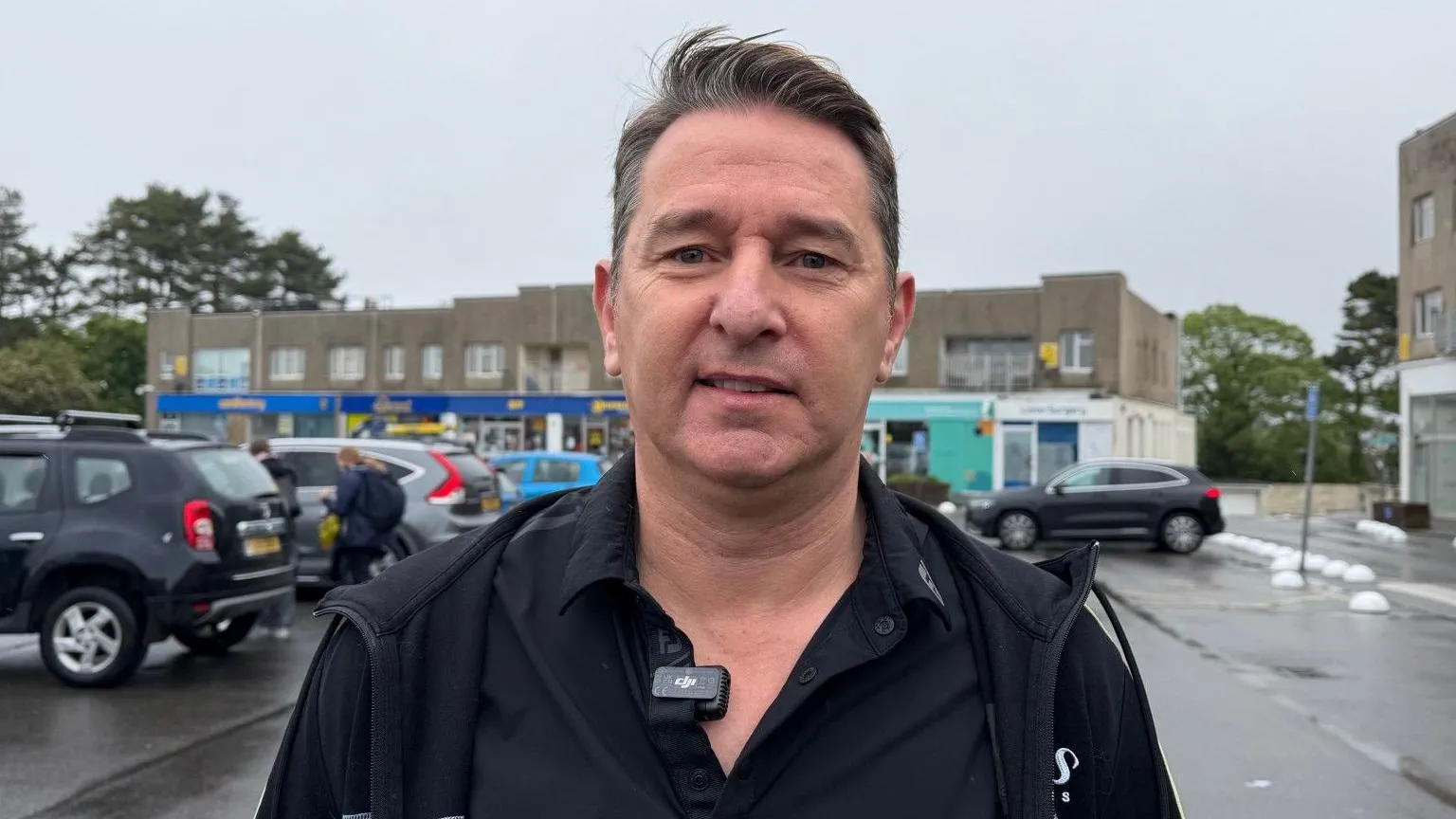 Joe Pinzari is wearing a black jacket and black T-shirt. He is pictured in front of Les Quennevais Parade. 