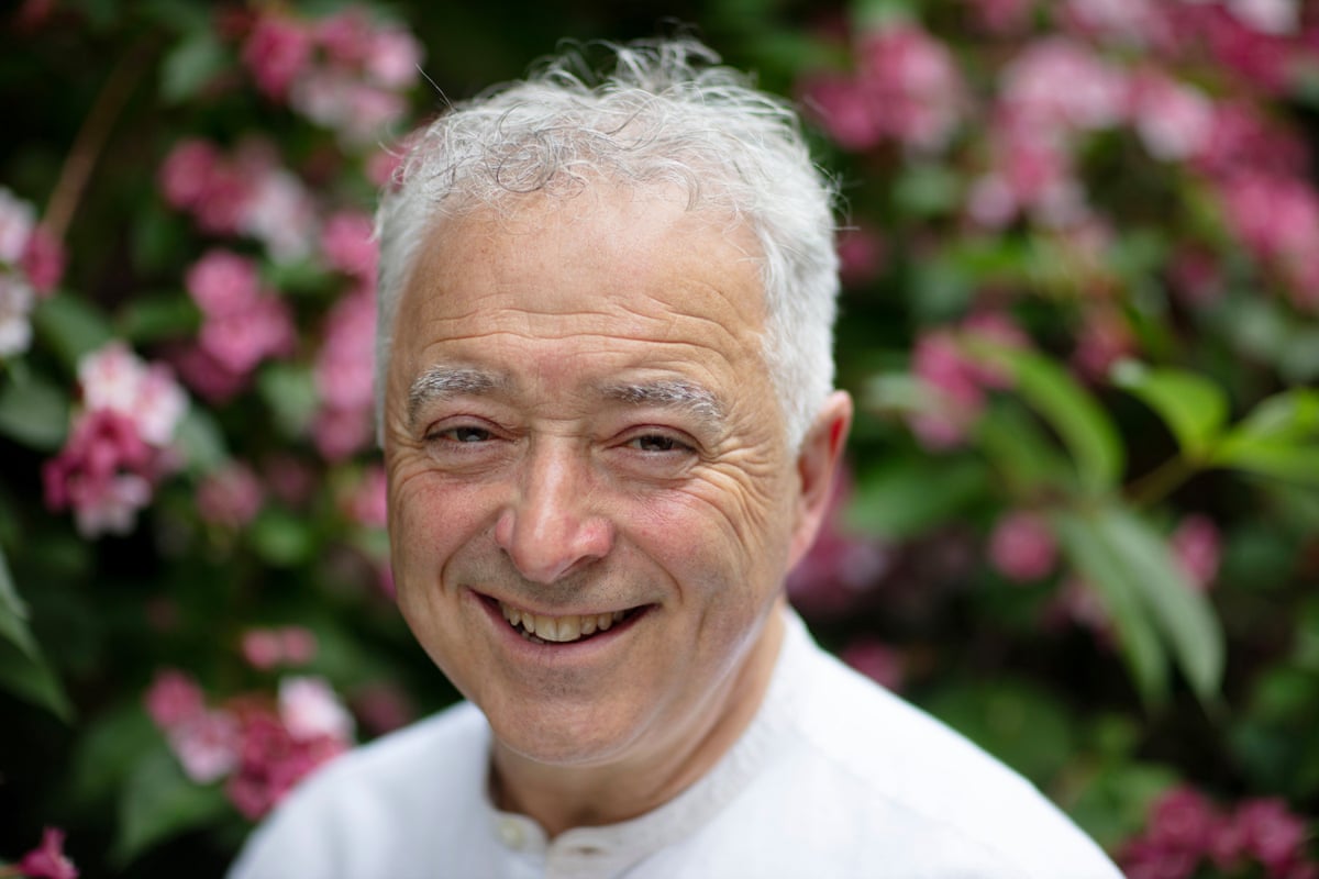 Frank Cottrell-Boyce smiling at the camera while stood in front of colourful flowers