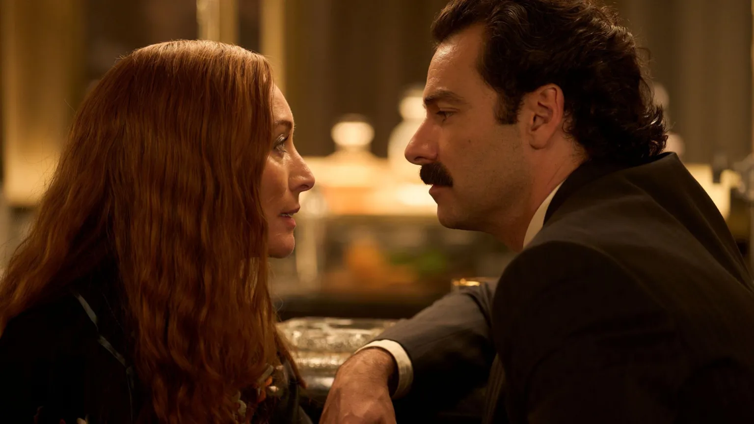 Robert Viglasky/Disney+ A shot from the series Rivals. It depicts the characters of Maud and Declan O'Hara looking at each other. Maud has long red hair and Declan has thick dark brown hair and moustache. 