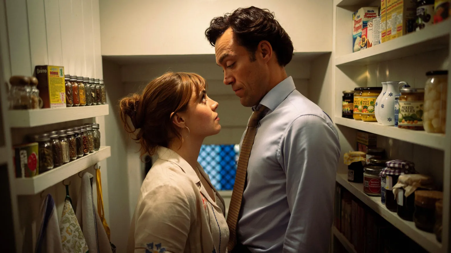 Robert Viglasky/Disney+ The characters Taggie O'Hara and Rupert Campbell-Black from the series Rivals. Taggie has brown hair tied up in bun, wearing a cream blouse. Rupert has dark brown hair, wearing a light blue shirt and brown tie. They are inside a pantry looking at each other. 