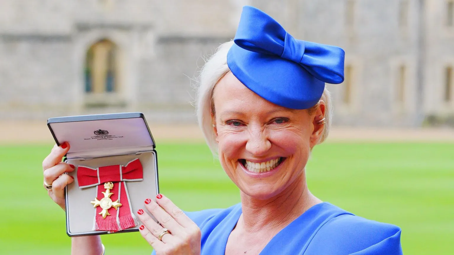  Ruth wearing a blue hat and dress holding her OBE