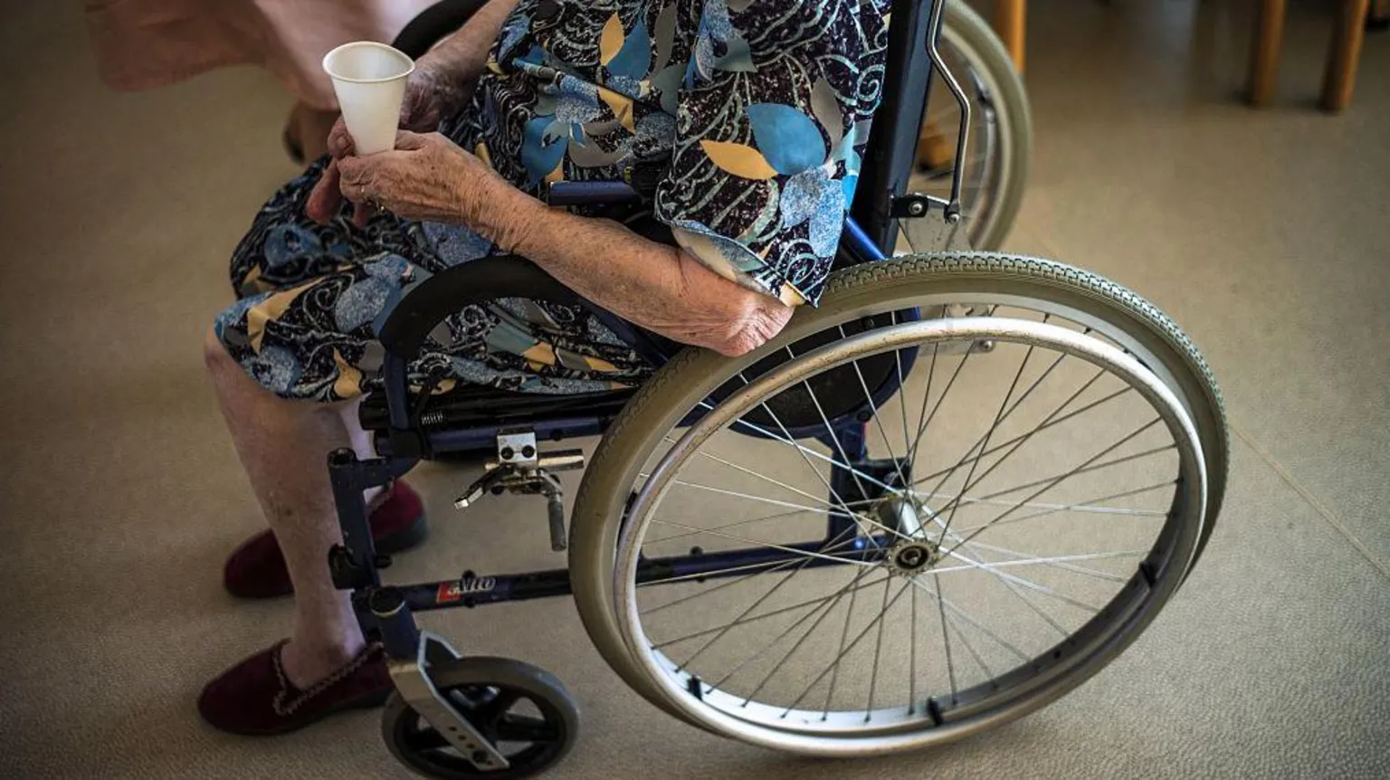 AFP via An elderly lady holding a plastic water cup sits in a wheelchair in a care home