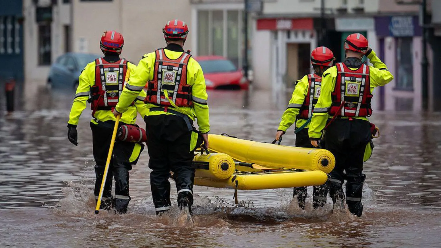 Matthew Horwood/ Fire service workers walk through water carrying an inflatable dinghy during flooding in Monmouth in November 2025