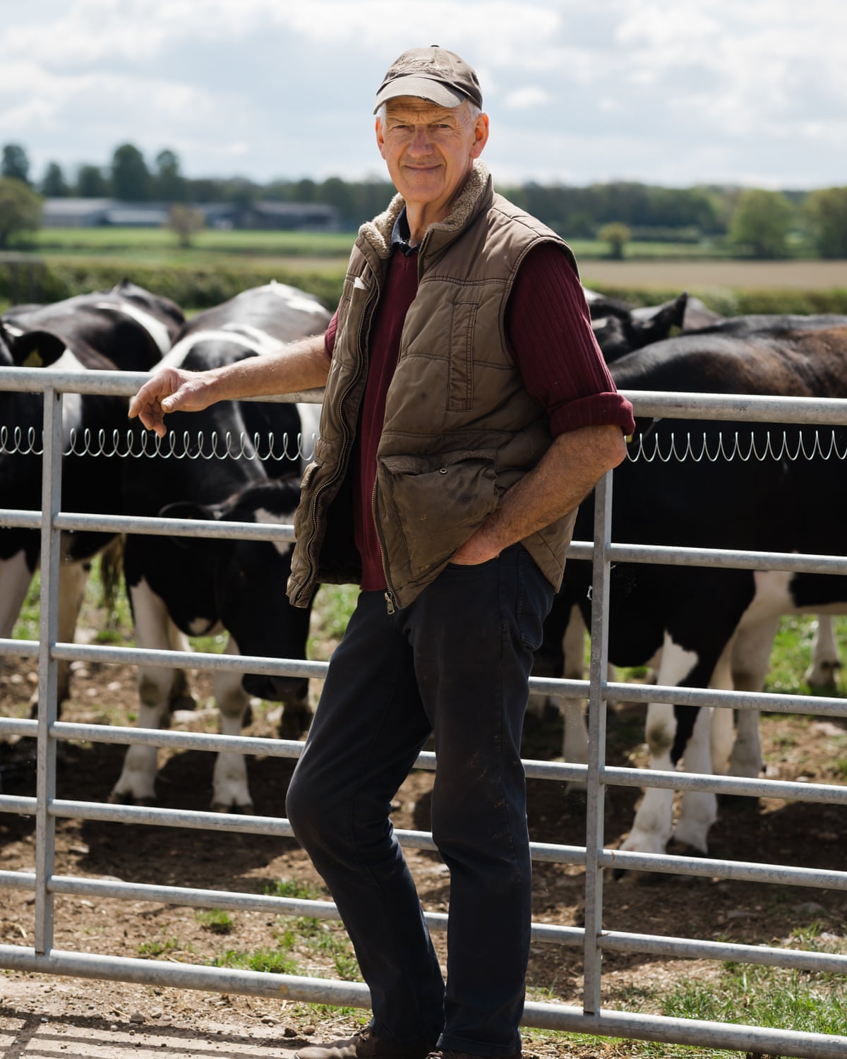 A male farmer stands alongside a gate behind which stand cattle