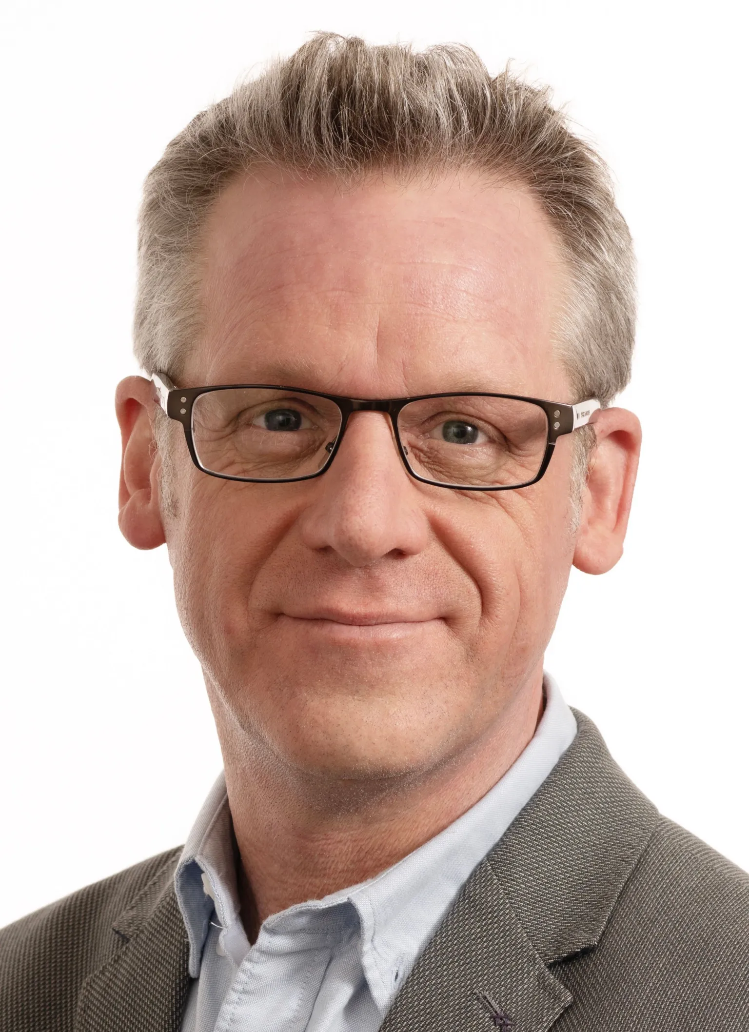 Mark Miller A man is looking at a camera with a white background behind him. He is in a shirt and blazer and is wearing glasses.