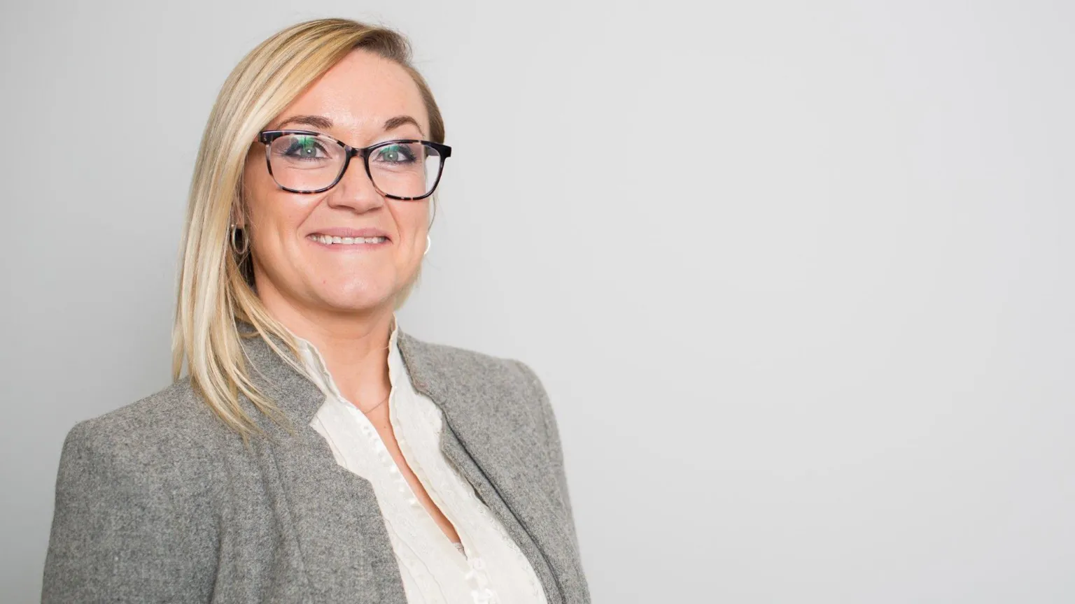 Advice NI Sinead has straight blonde hair parted to the side and falling onto her shoulder. She is wearing glasses, a grey coat and a white top. 