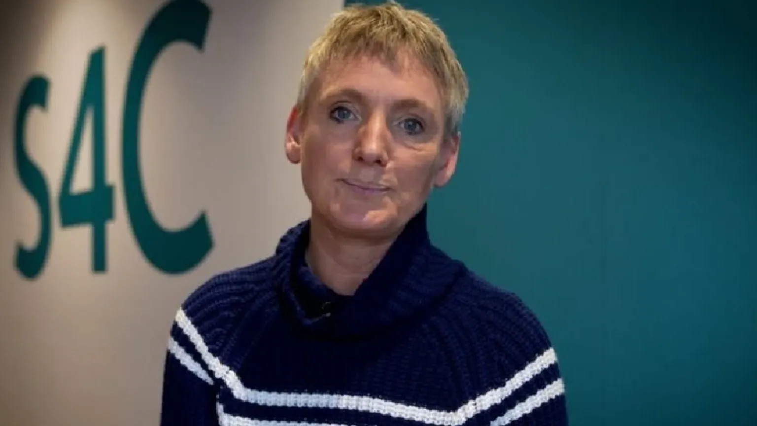 Sian Doyle wears a black jumper with two horizontal white stripes. S4C is written on the wall behind.