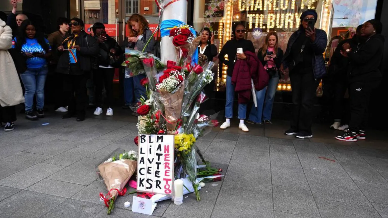  A flower memorial on a lamppost. A sign that says 'black lives matter here too' is at the front.