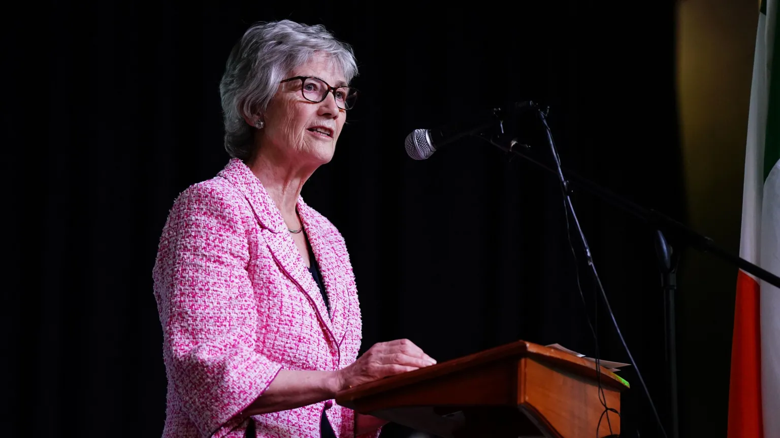 Irish president Catherine Connolly speaks during a visit to the Leeds Irish Centre, as part of her official visit to the UK. She has short white hair wearing glasses and a pink tweed jacket. She is standing at a podium giving a speech.