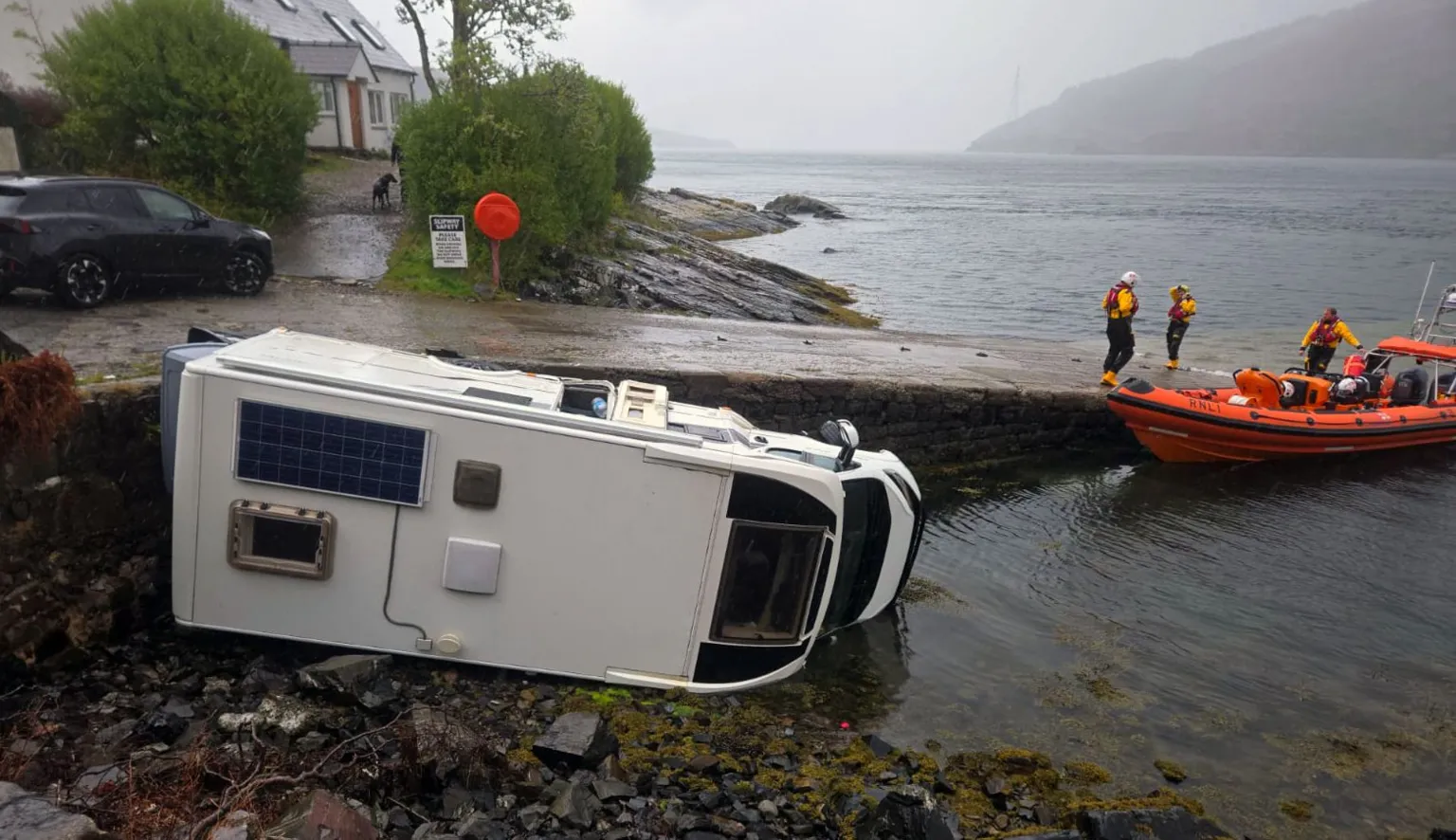 Kyle RNLI A white campervan lying on its side beside a slipway with an orange lifeboat in the right of the picture