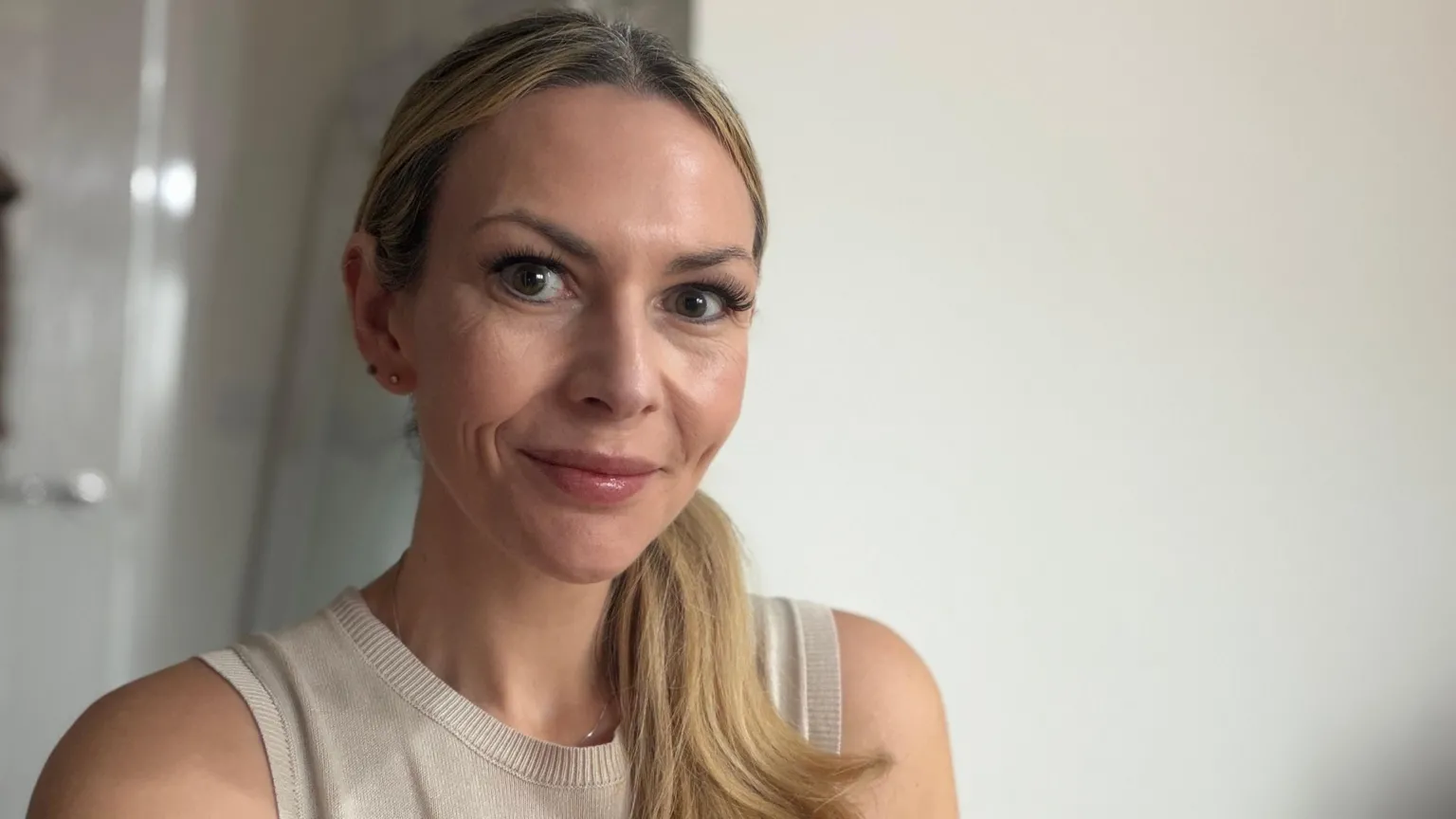 Aimee Bradley A head and shoulders shot of a white woman with long blonde hair in a ponytail over her left shoulder who is smiling at the camera. She's wearing a beige vest top.