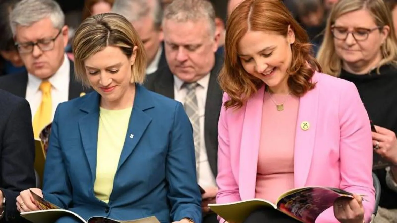  Jenny Gilruth, with a blonde bob wearing a blue blazer and yellow blouse. Sitting beside her is Màiri McAllan who has copper hair and is wearing a pink blazer and blouse.