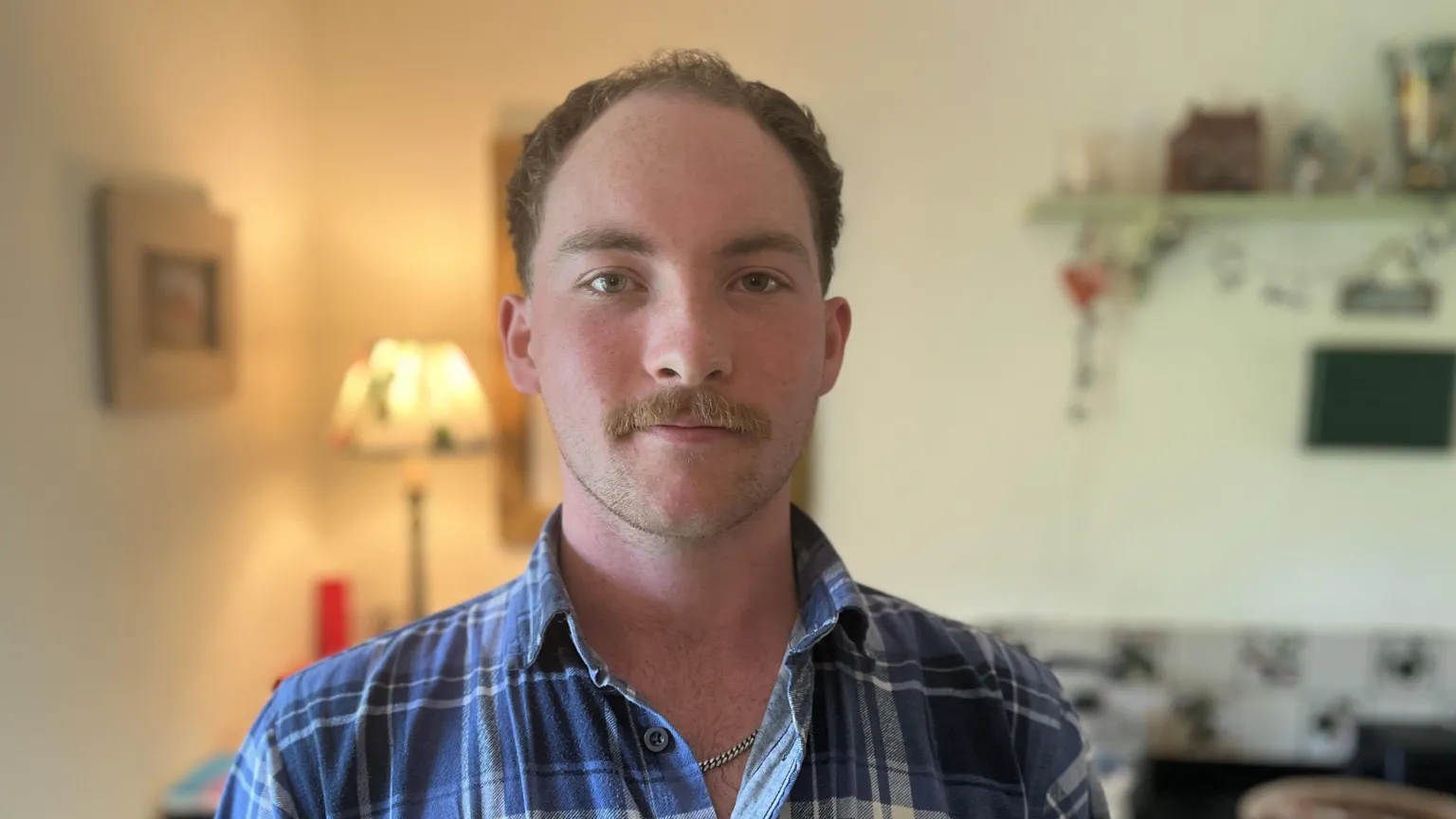 A man with short brown hair and moustache looks at the camera