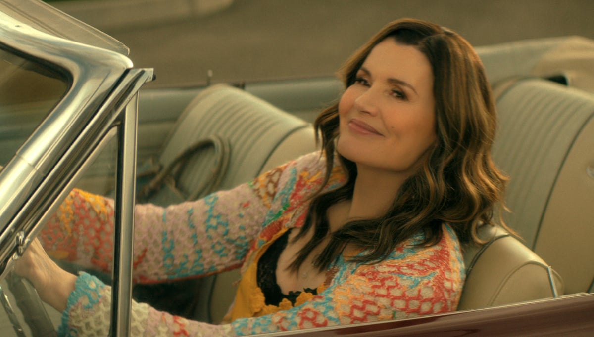 A woman smiling, wearing a patterned shirt, in a car with the roof down