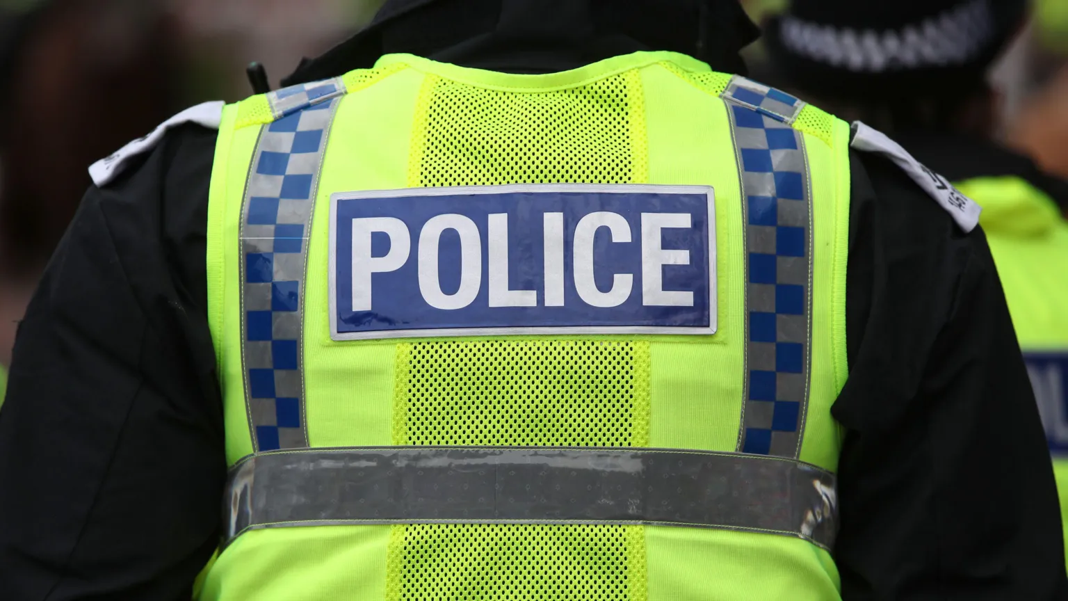 A Police Scotland officer facing away from the camera with the word police on the back of a hi-viz vest.