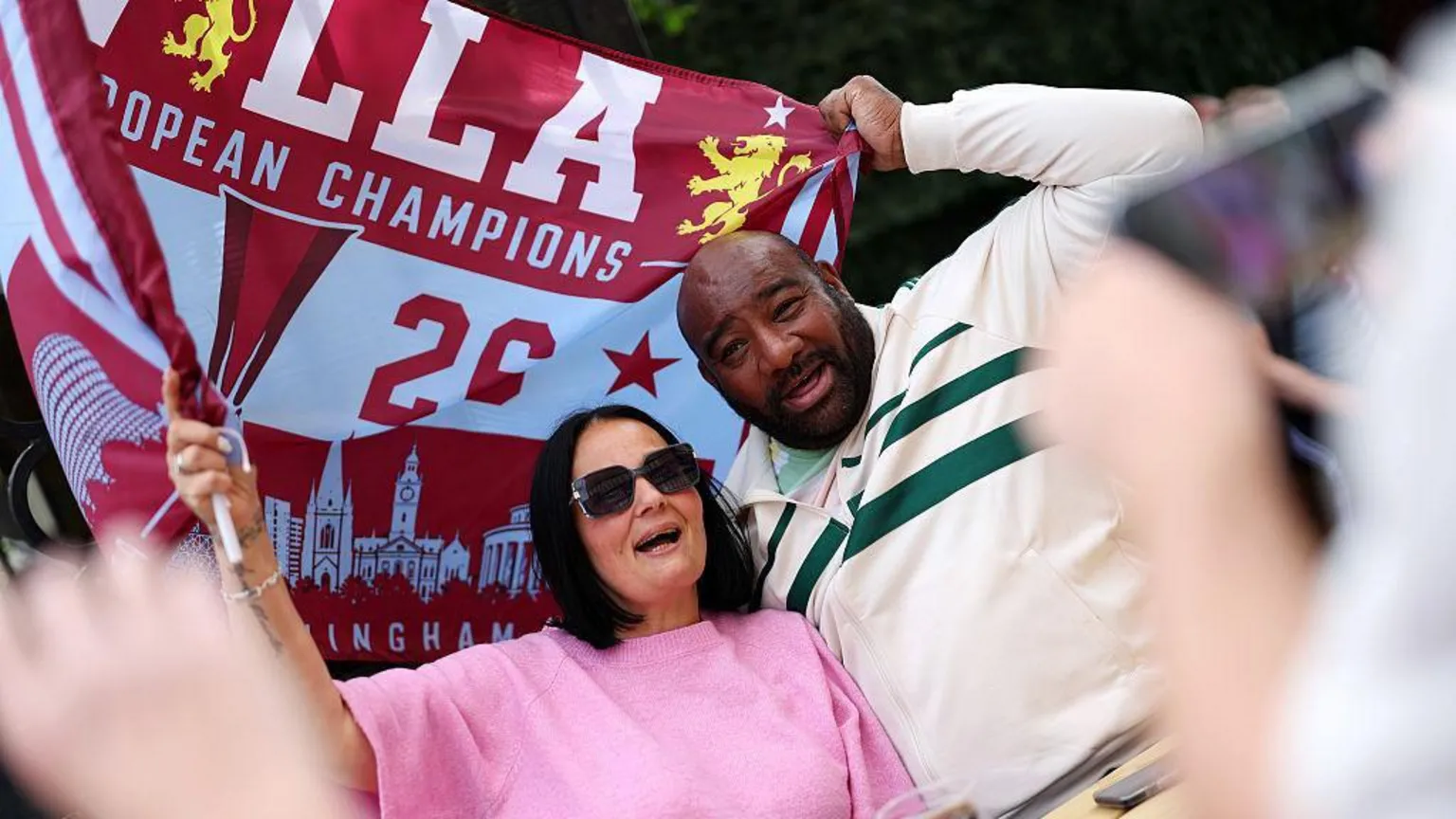 Two Aston Villa fans hold a flag above them during the parade.