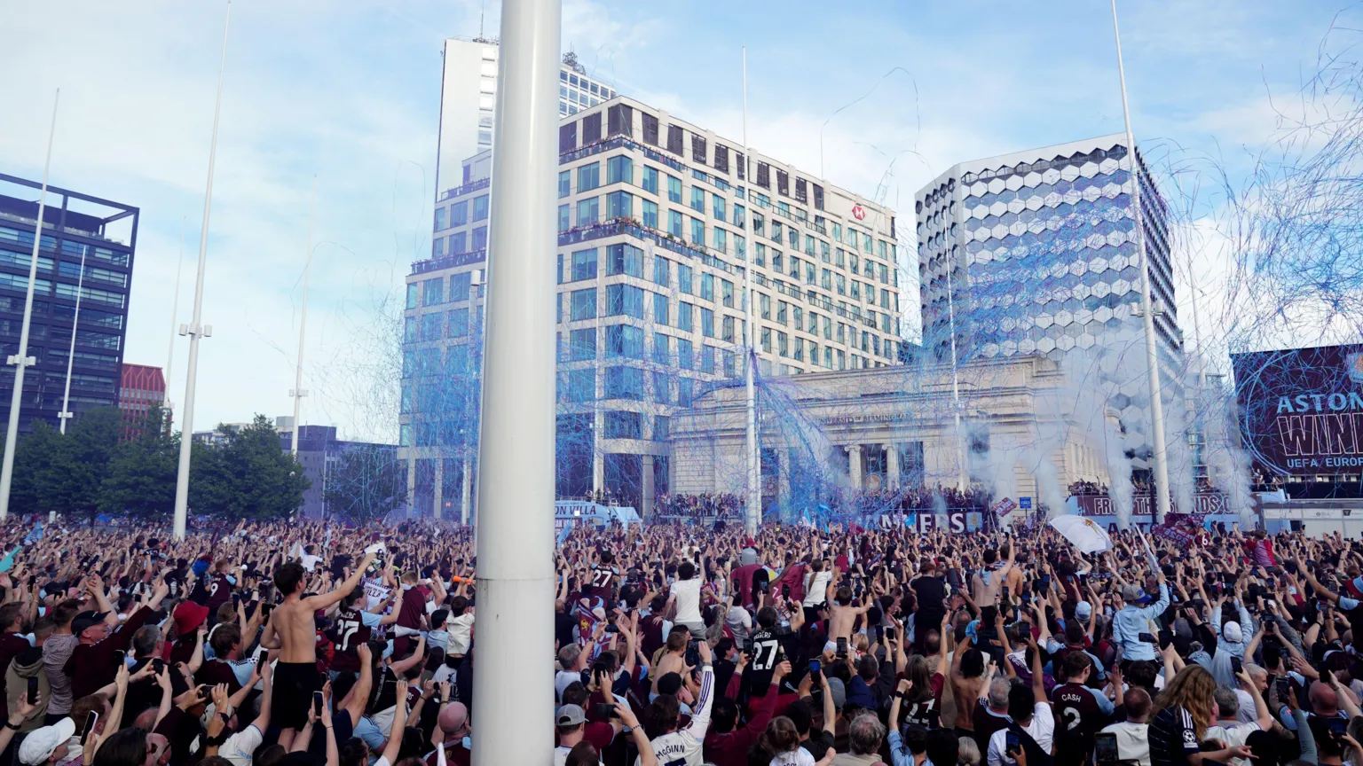 A large crowd of fans packed into a city centre square as blue ribbons and streamers are shot into the air.