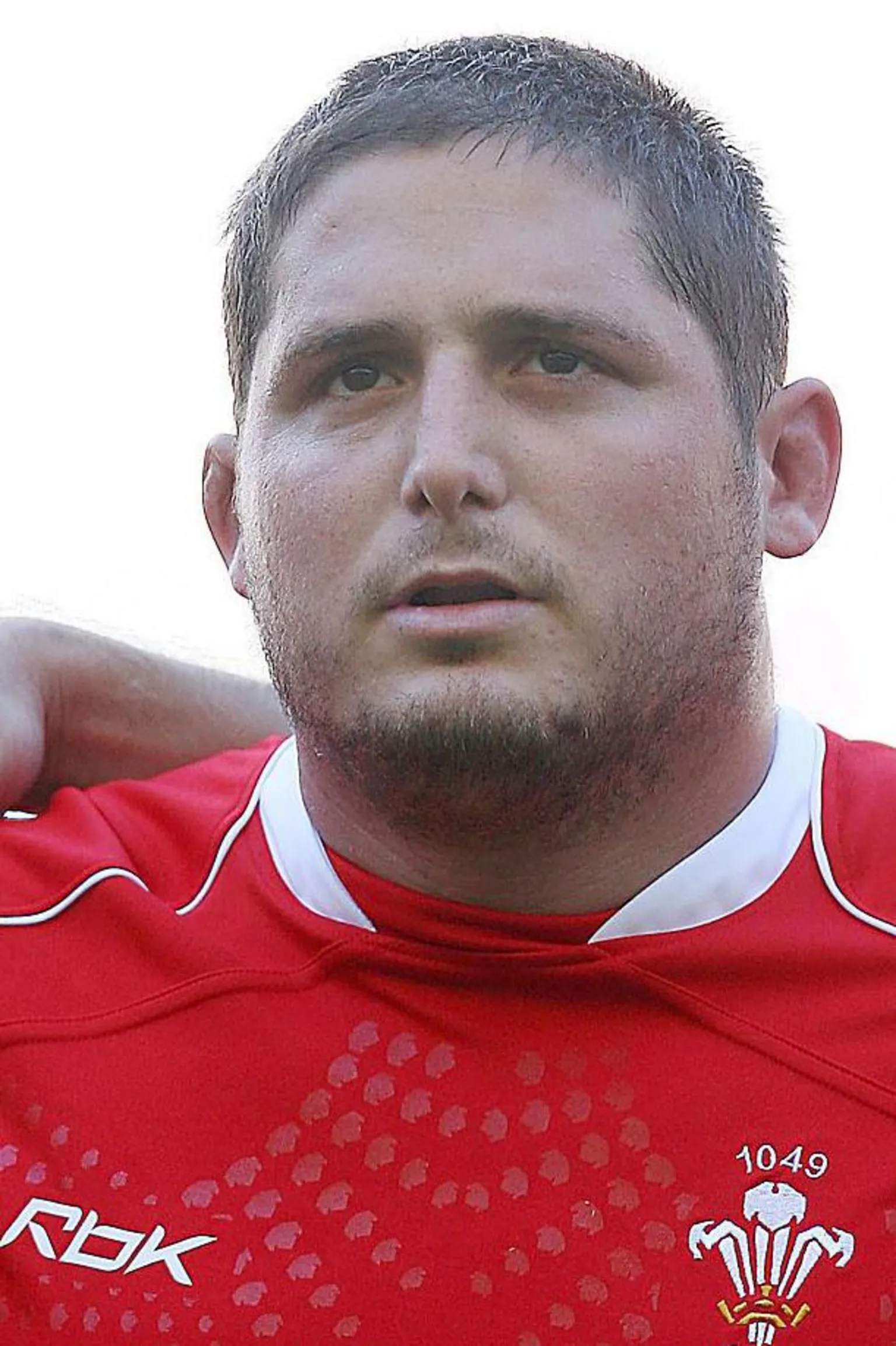 Rhys wearing his Welsh rugby jersey singing the national anthem. He has a serious look.