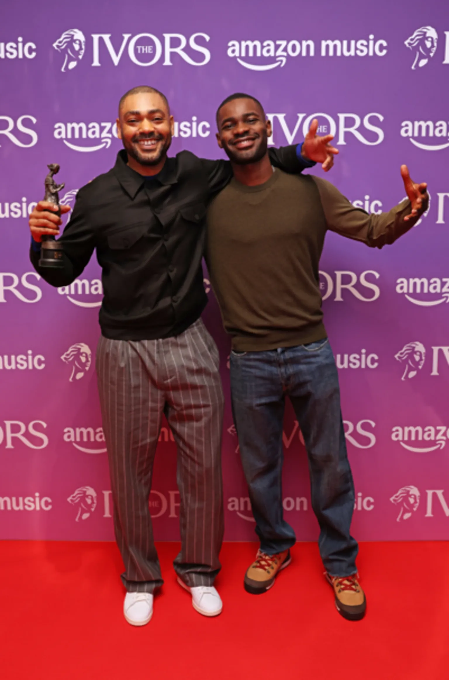 Kano and Dave smile and stand on the Ivors red carpet. Kano holds his Ivor Novello Award.