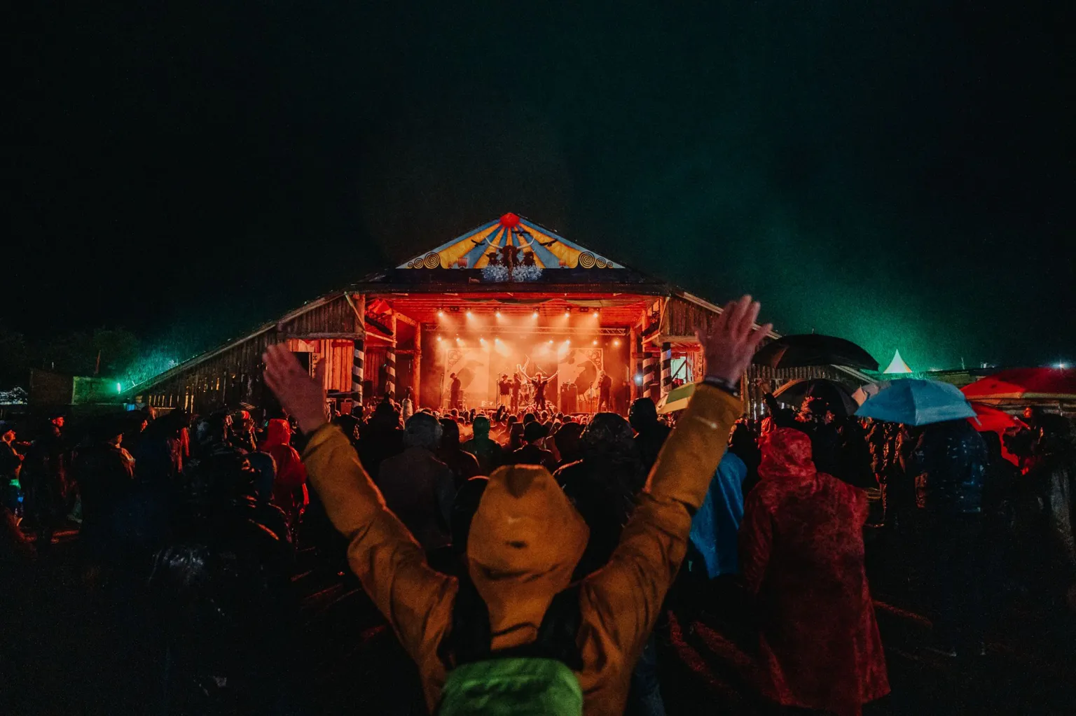 Recompose A brightly lit stage viewed from a distance with a fan standing close to the camera with their hands up in the air