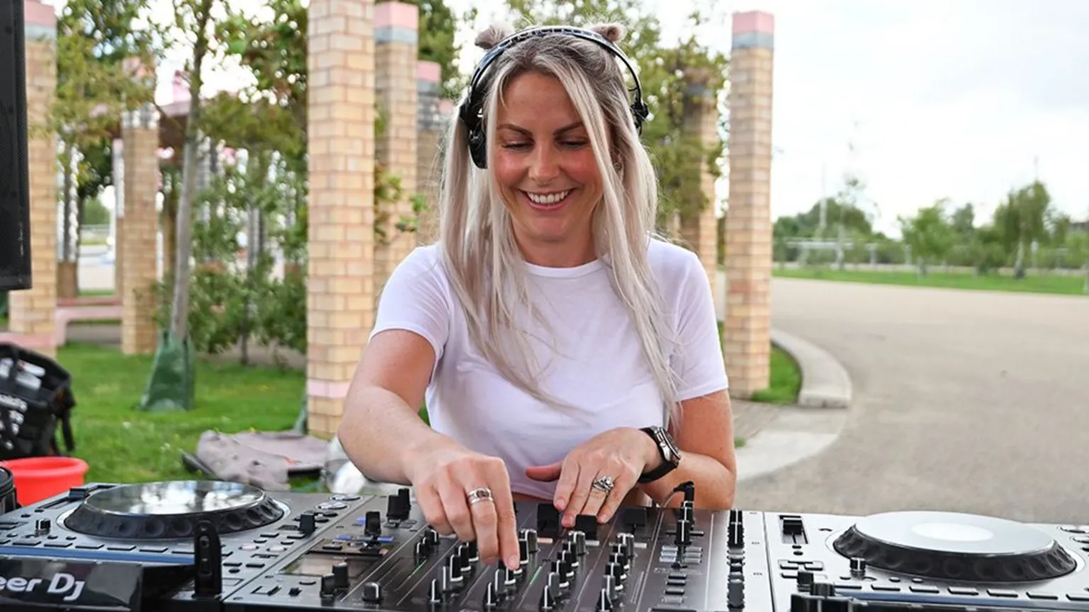  DJ Charlie Hedges, a female, wearing a white tshirt and headphones, as she DJs on black decks.
