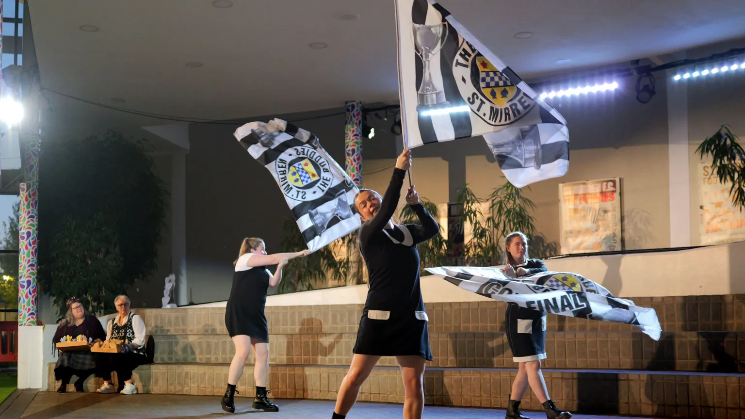 Sartorial Pictures Three performers onstage during a Paisley Opera production of Carmen. They are moving about and waving St Mirren flags.