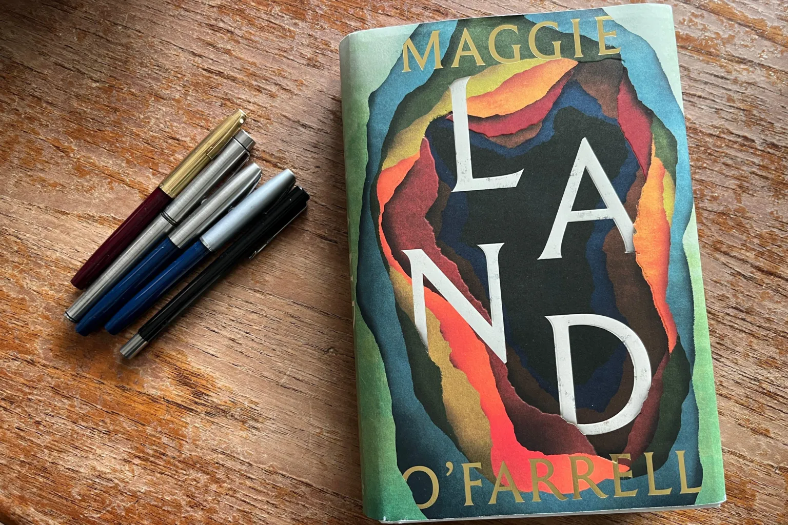 BBC/Katie Razzall 5 fountain pens on the left and copy of her new book Land on the right front cover has bright colours of red, orange, blue and green