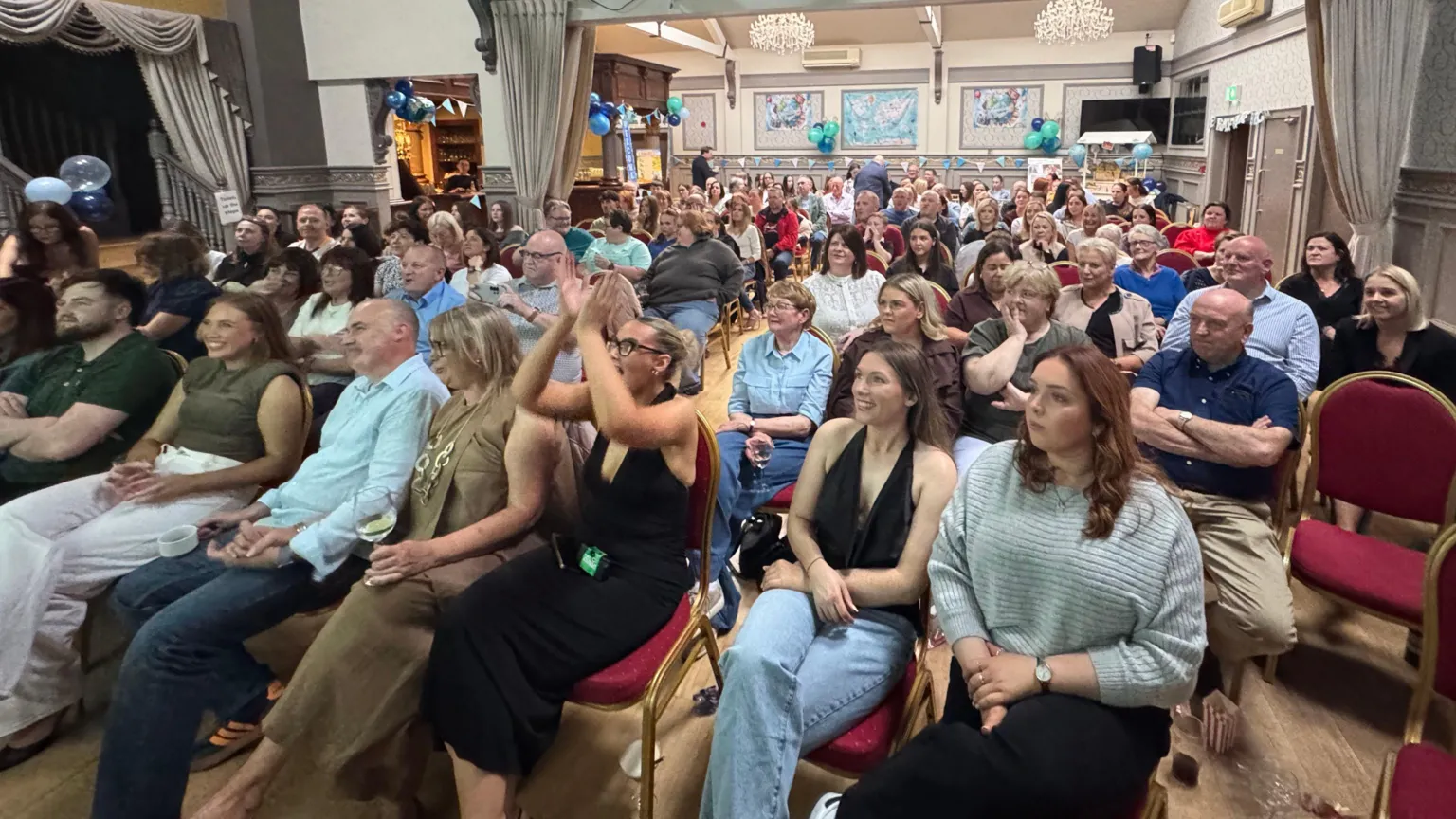 Crowds of people inside a function room sitting on chairs all facing forward.