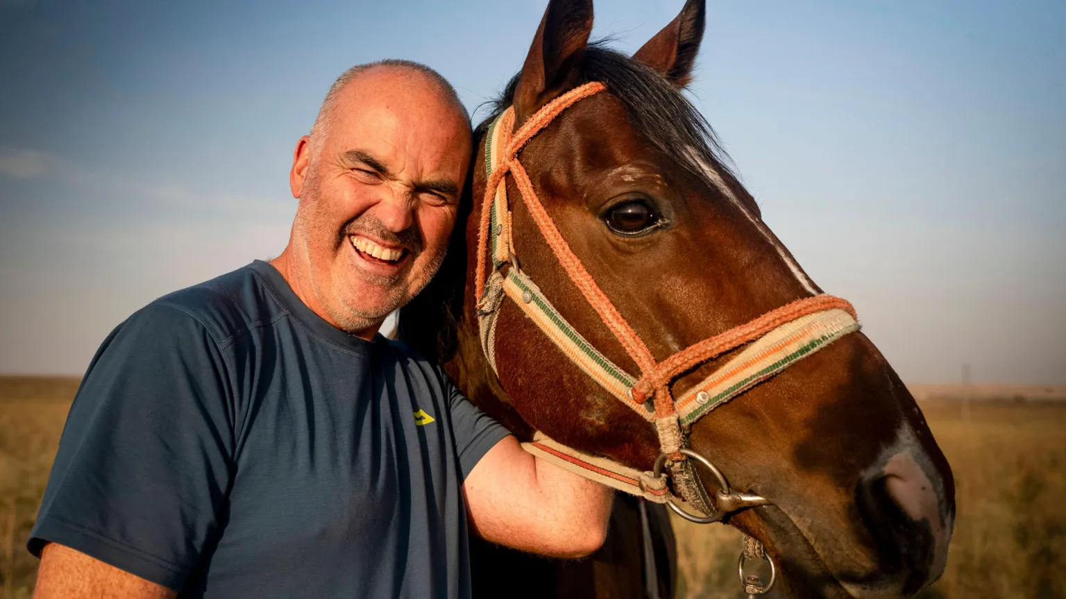 BBC/Studio Lambert Andrew with is arm wrapped around the head of a horse. He is bald and wearing a blue t-shirt.