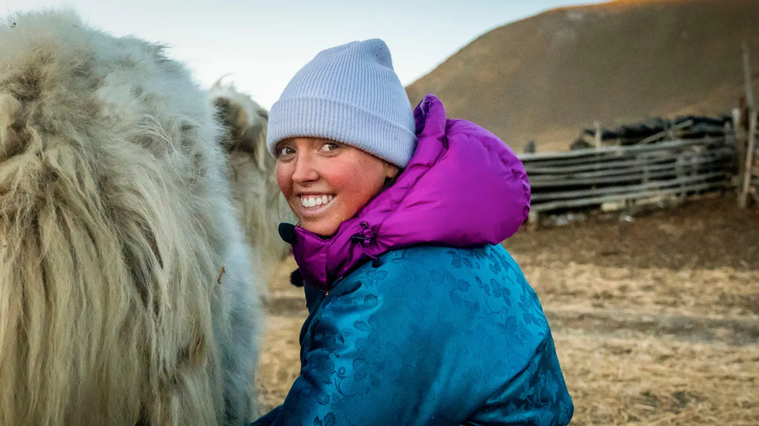 BBC/Studio Lambert Molly standing beside a large fluffy animal. He is wearing a light blue beanie, blue coat with pink hoodie underneath.
