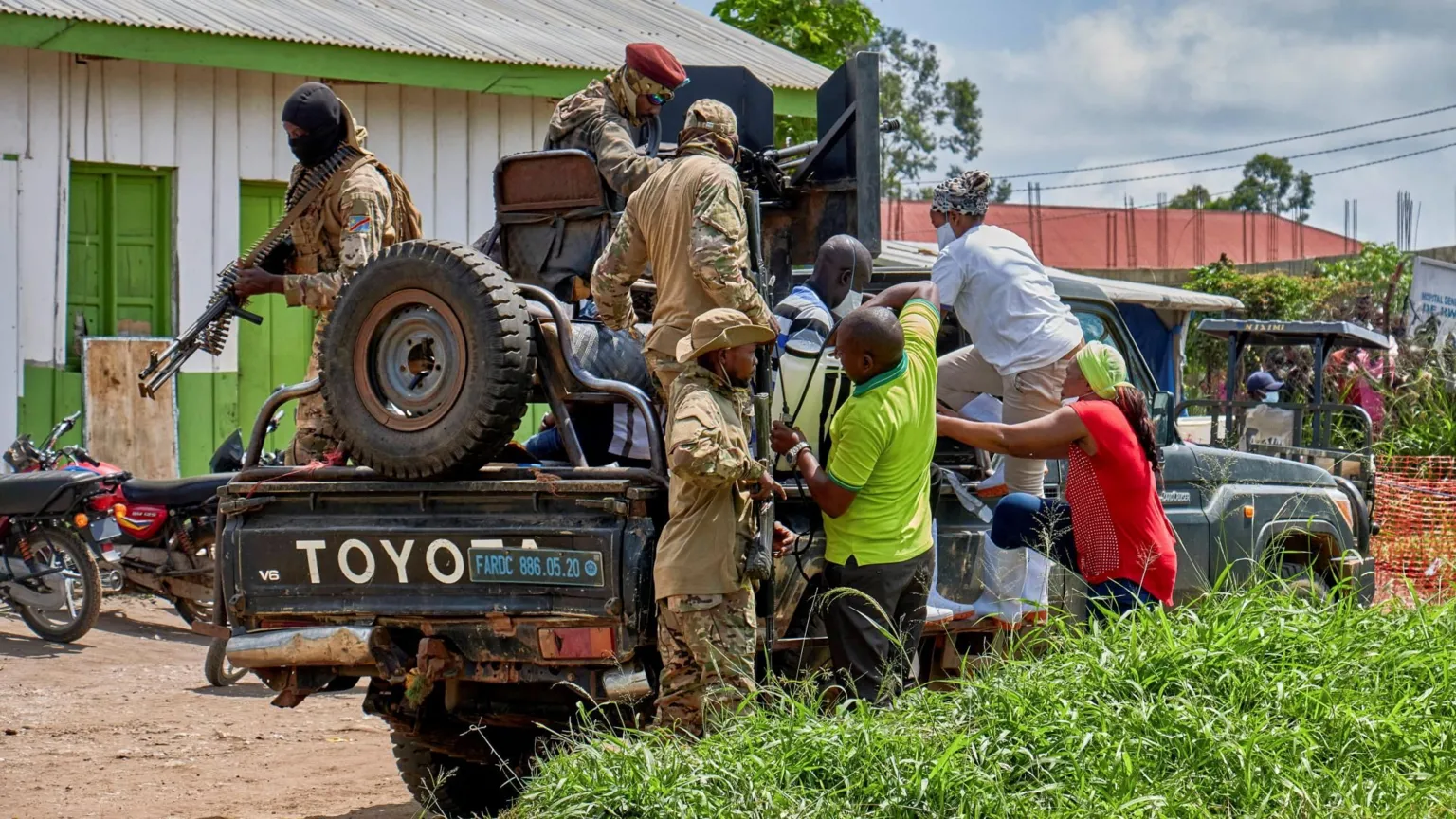  Medical staff climb aboard a military vehicle on the grounds of Rwampara General Hospital. One soldier pictured in camouflage has a large machine gun.