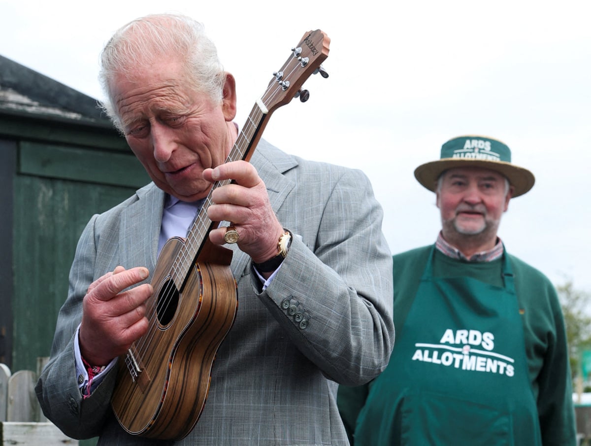 King Charles plays the ukulele watched by an onlooker