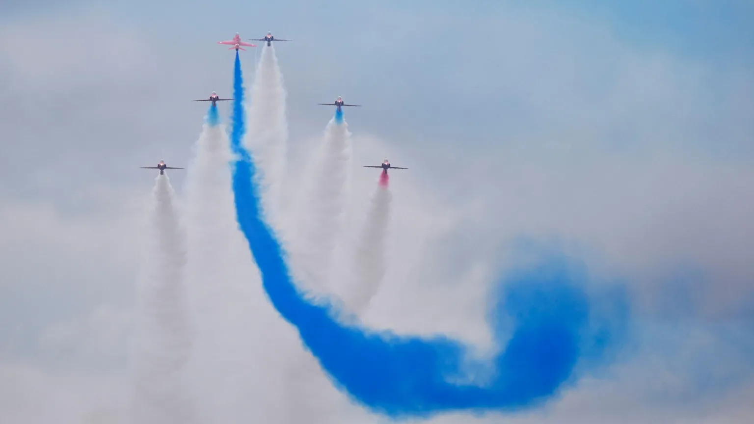  Planes are seen in the sky with colourful condensation trails left behind in the sky. The main colour is blue, others are white.