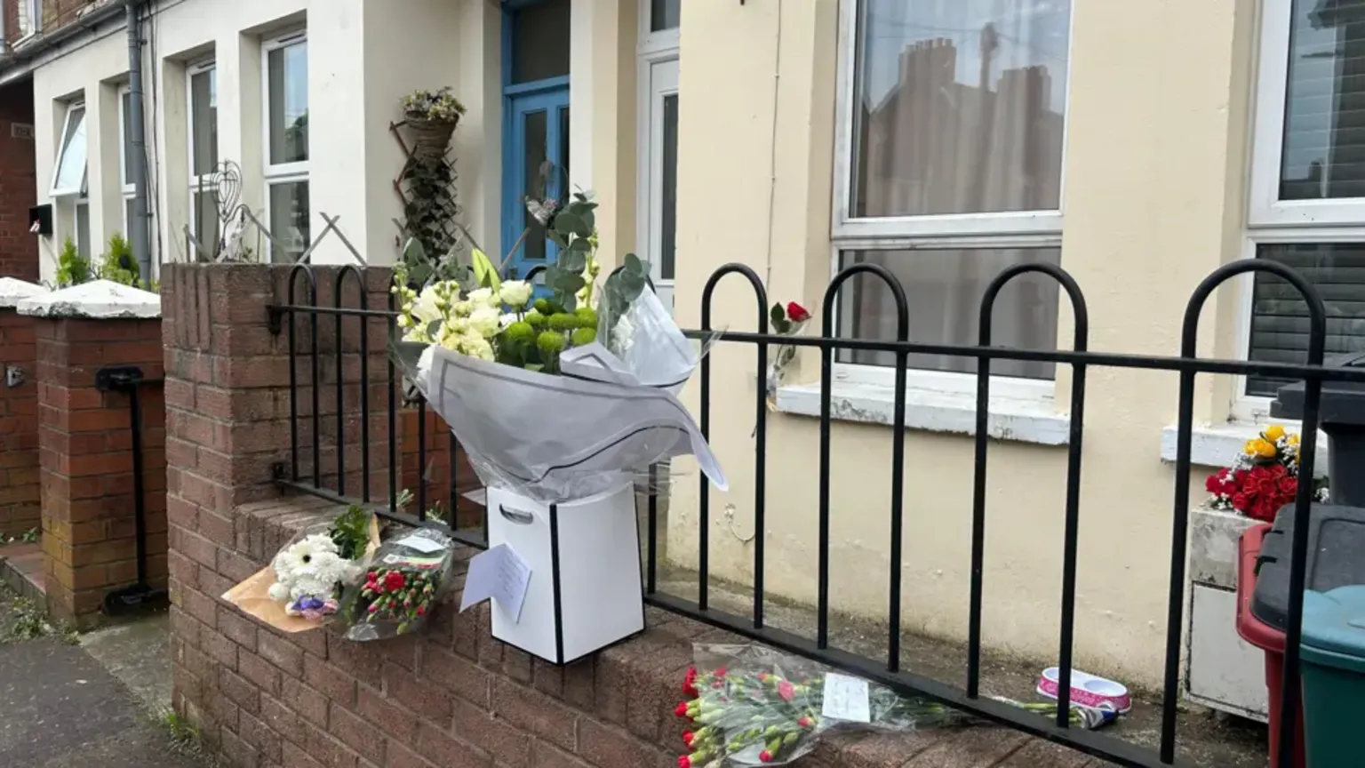 Bouquets of flowers siting on a wall outside a terraced house.