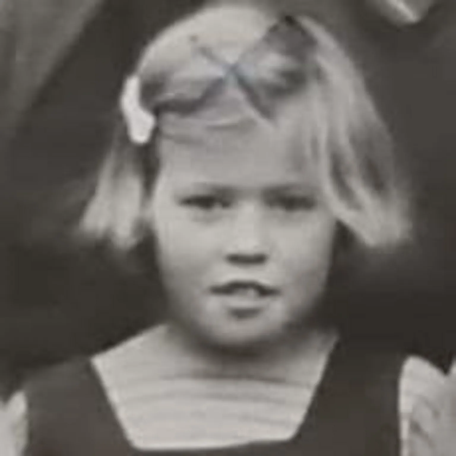 Fiona Brown A black and white photograph of a child Moira with short fair hair, and a bow clip on the left. 