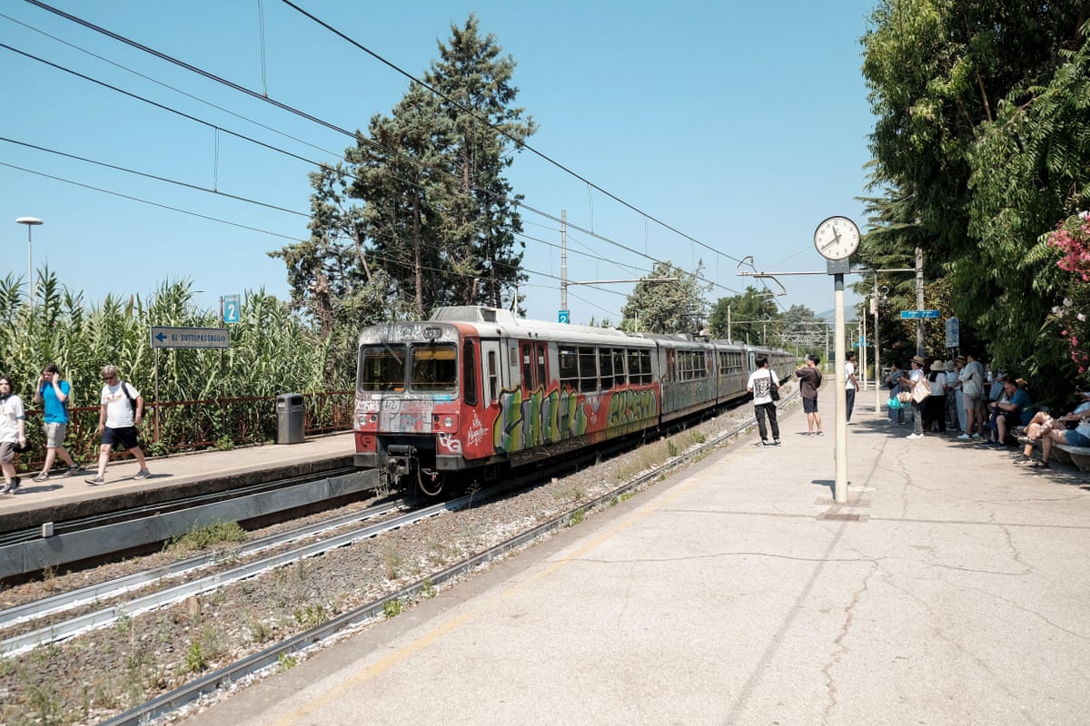 A graffitied train stops at a station under a clear blue sky.
