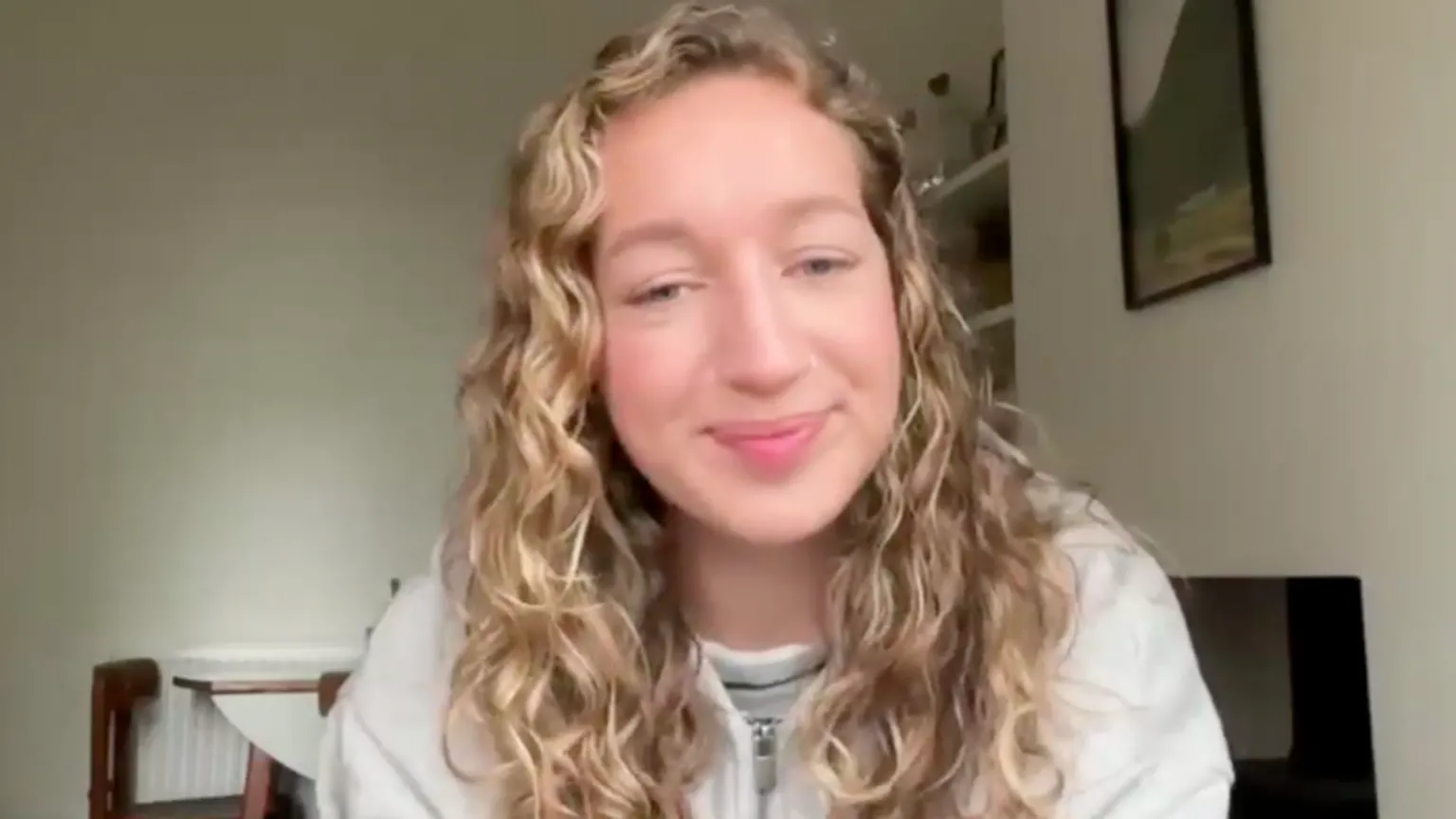 a girl with long, blonde, curly hair smiles at the camera.