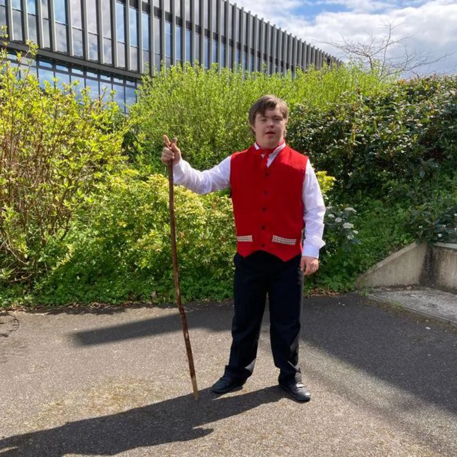 Sion holding a stick and wearing a red waist coat