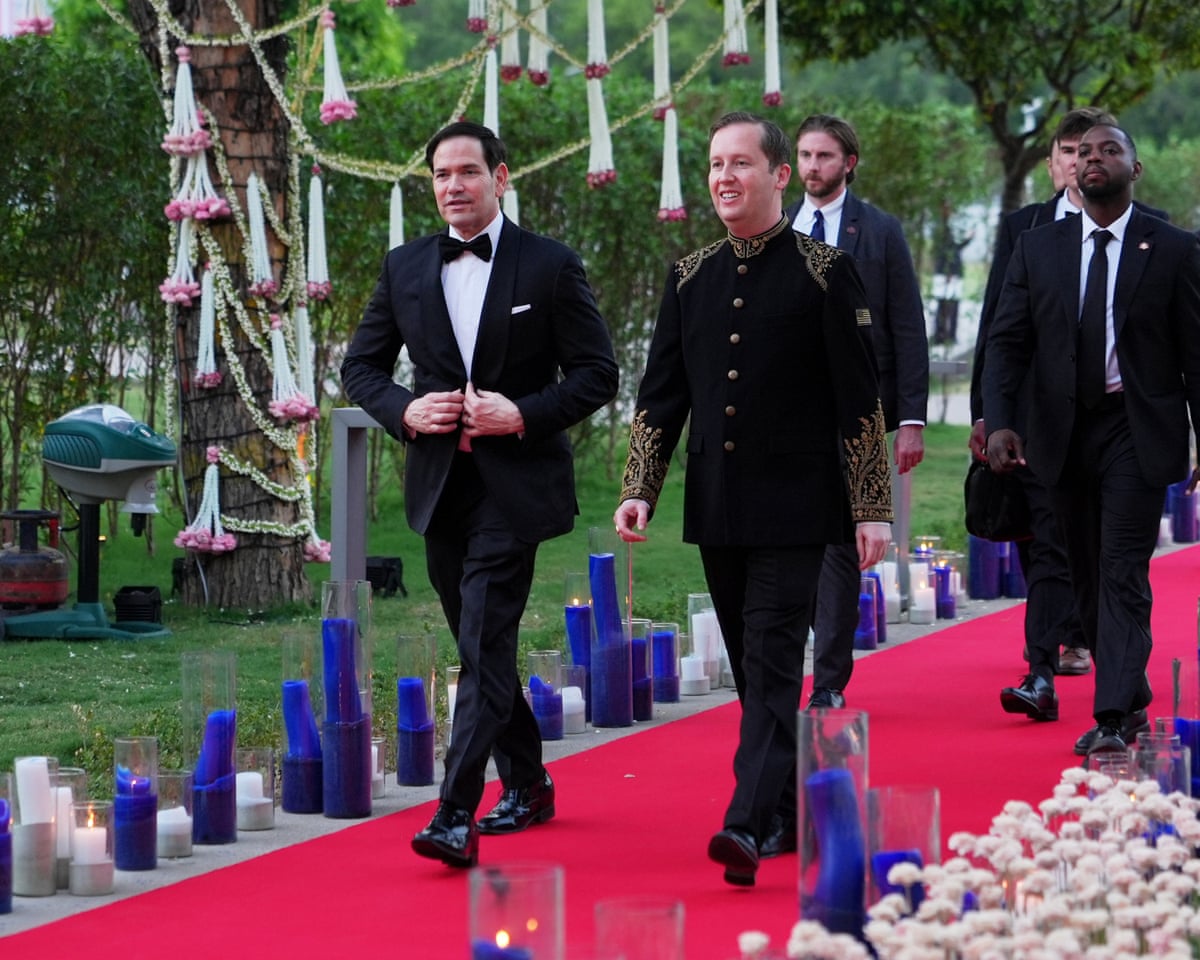 Marco Rubio walks with a group of people along a red carpet outdoors