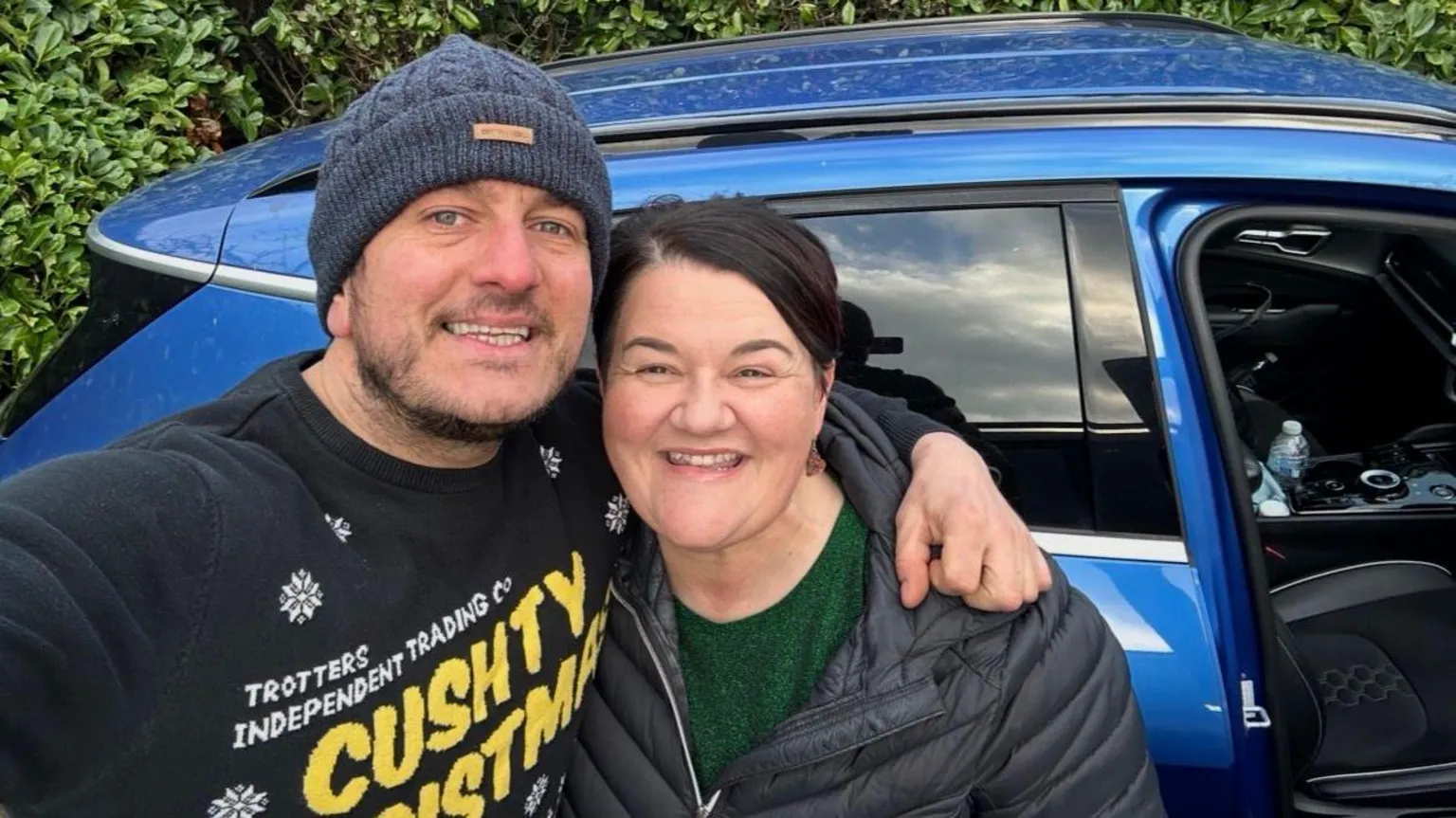 Andy Bennett, pictured left, holds a phone in one hand as he takes a selfie with Emma. He has one arm around her shoulder and wears a black Christmas jumper and a navy-blue hat. Emma has short brown hair and smiles at the camera. She is wearing a dark-green top underneath a black puffer coat.