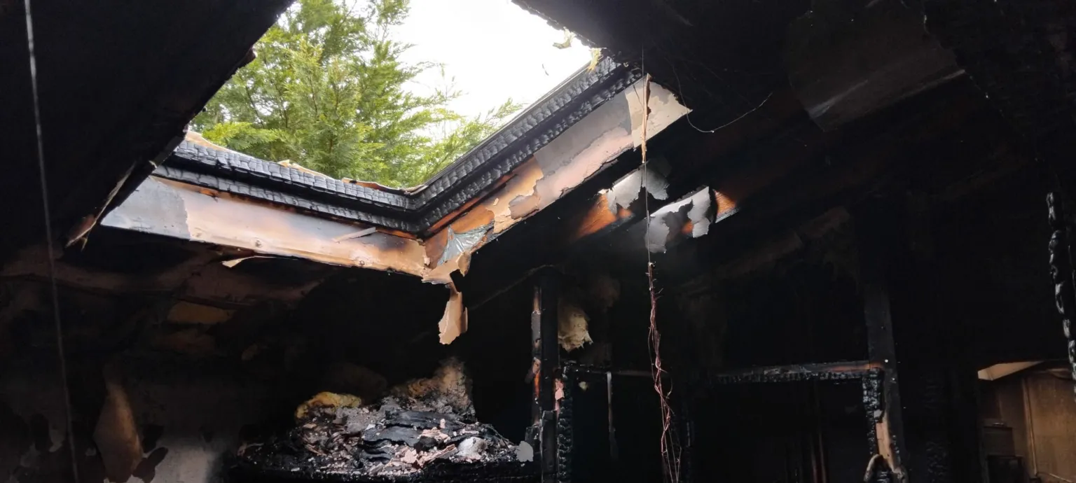 Tom Elliott The ceiling around an open skylight is charred and black. Debris hangs from the ceiling.