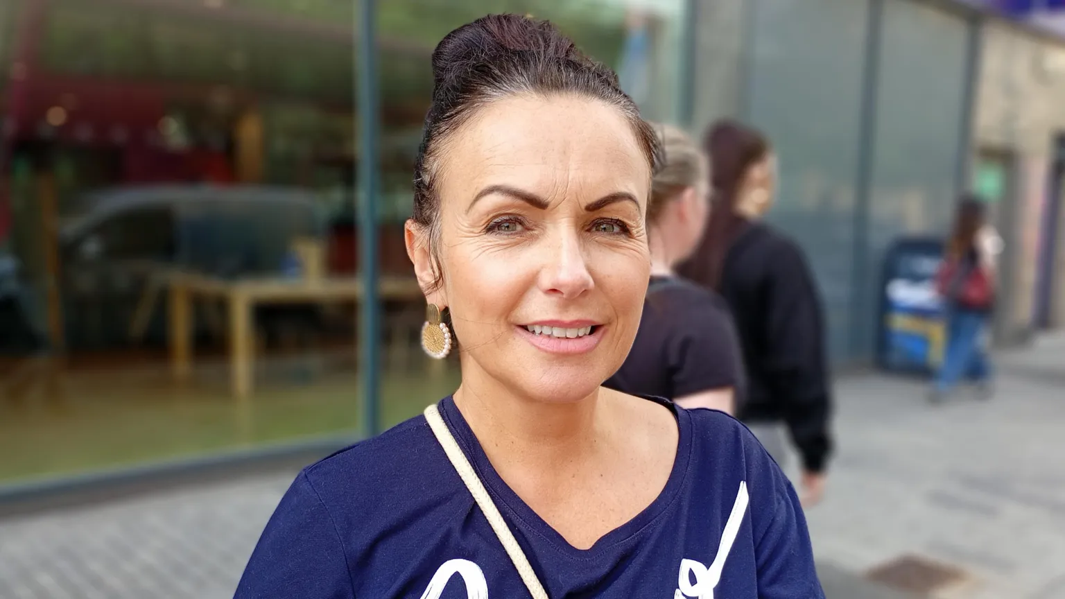 A woman, with brown hair tied up, wearing a navy top. She is looking at the camera.