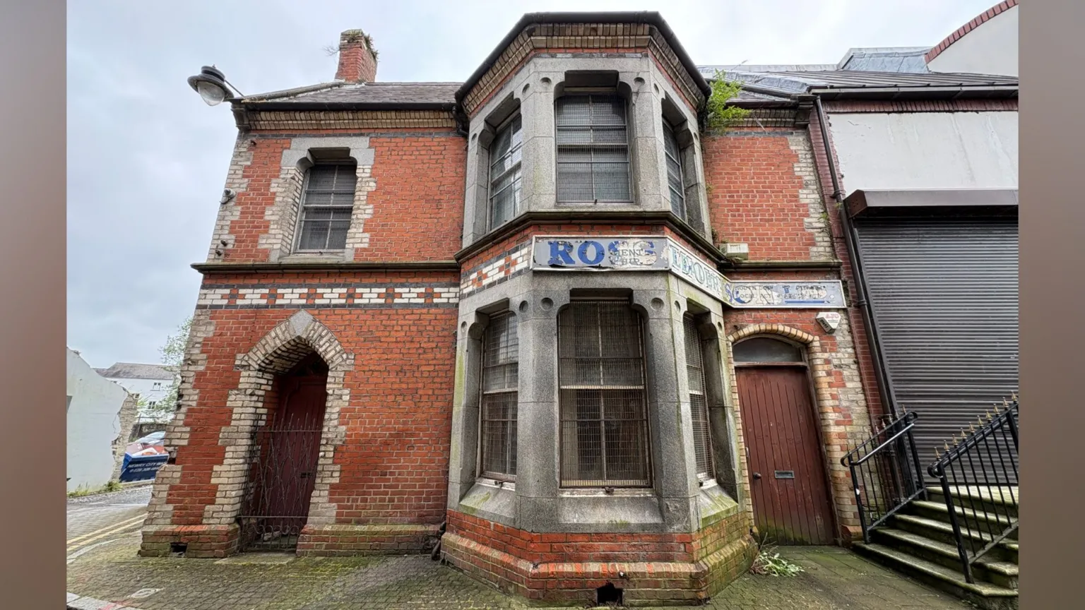 No 2 Bank Parade - an end-of-terrace red brick house with a double-storey bay window and two arched front door entrances. A band of decorative yellow, black and white bricks intersects the front elevation between the ground floor and first floor.