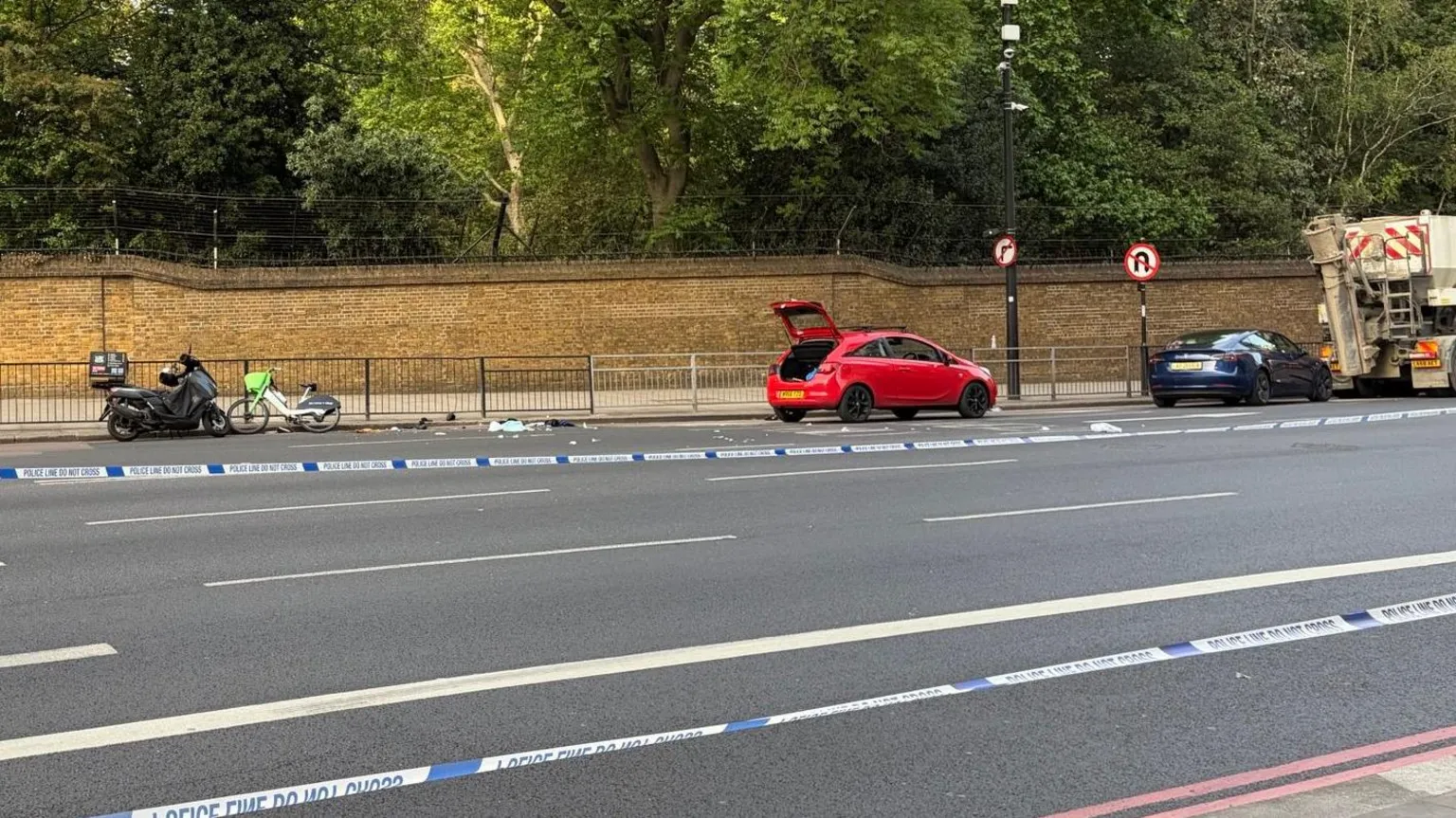 A Lime bike, moped, two cars and a cement truck seen parked on a road behind police tape. One of the car boots is open.
