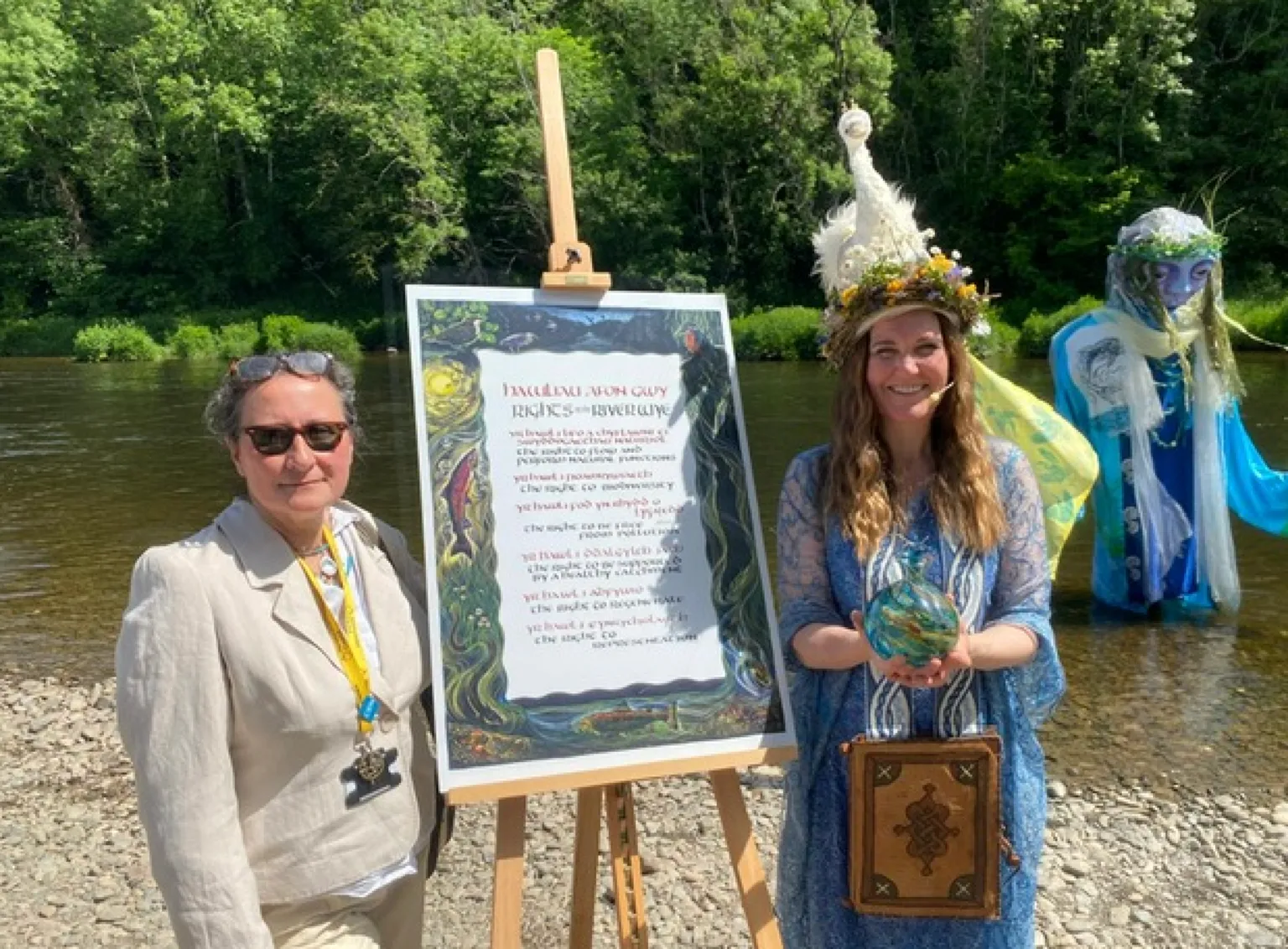Two women stand either side of an easel on which the charter stands. One wears a linen suit, the other wears a long blue gown