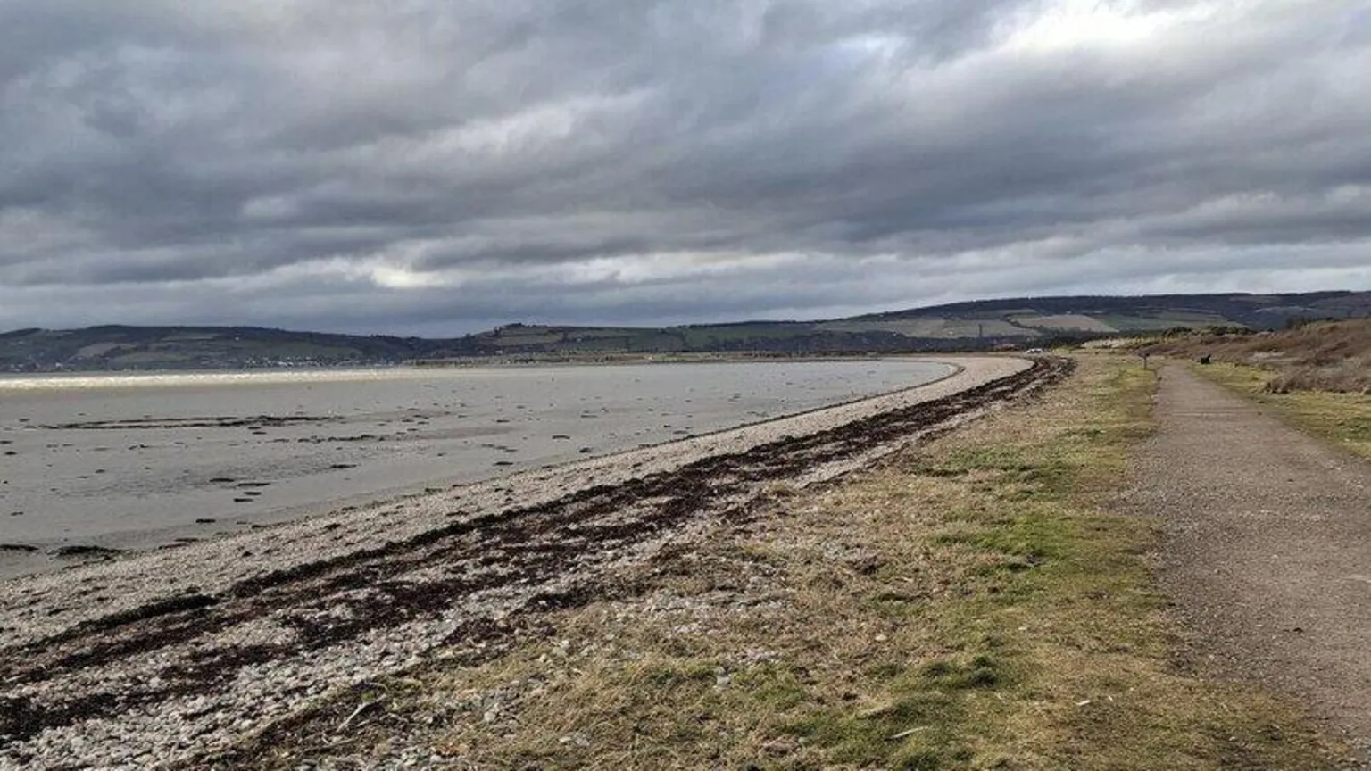 MikePennington/Geograph The common is close to the sea. It is a flat area with a path. The tide is out revealing a long strip of shingle.