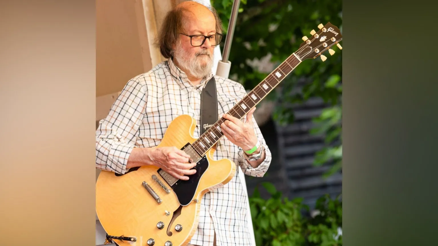 Mike Sandford A man plays guitar. He is in a white shirt and has glasses and a big grey beard.