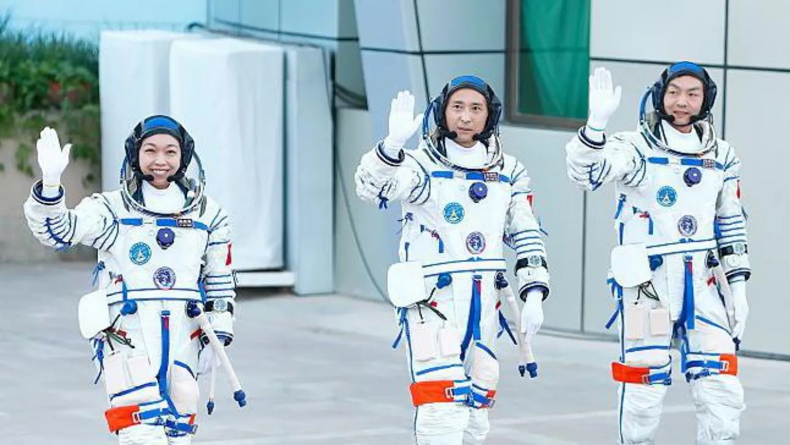  Three Chinese astronauts wearing white space suits wave in front of a jubilant crowd waving Chinese flags ahead of the Shenzhou-23 launch