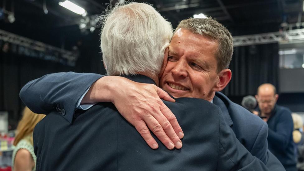 Edward a'i fab Rhun ap Iorwerth yn cofleidio yn ystod y cyfrif etholiadol ym Mai 2026