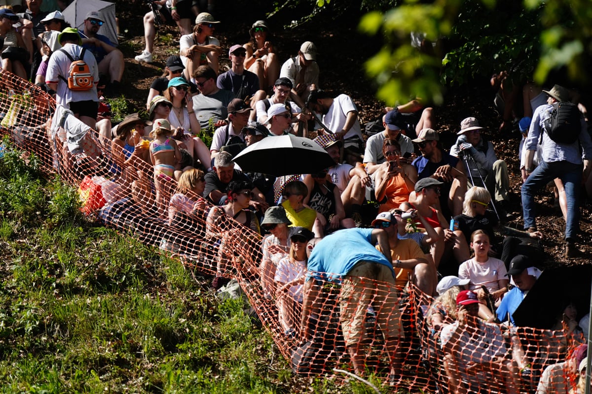 Crowds behind a plastic fence, with umbrellas, trying to stay in the shade